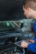 Male mechanic using digital tablet while examining car engine