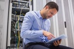 Man using tablet pc beside servers in data center